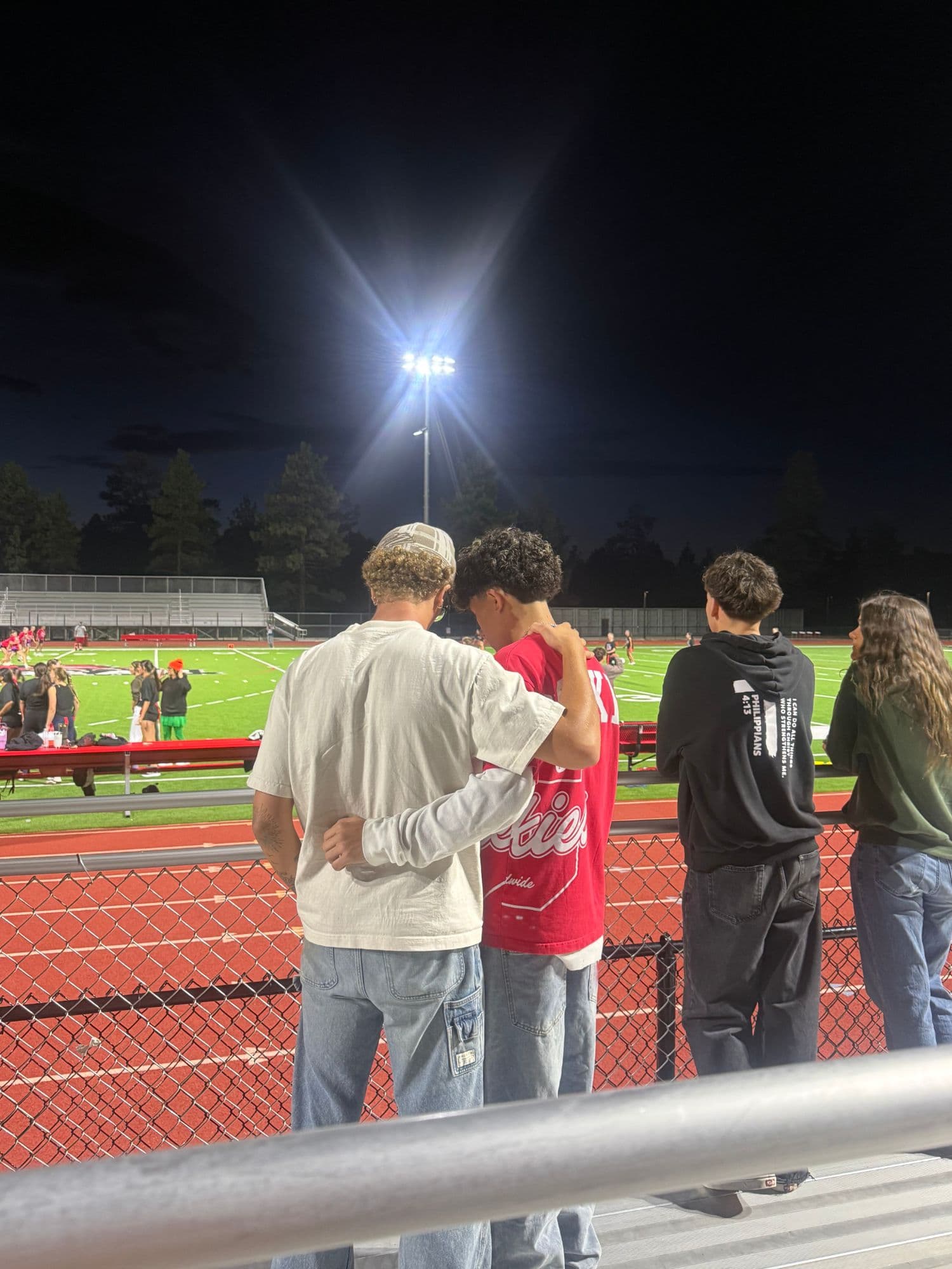 A youth leader with his arm around a student, watching a Big Bear High School game under the Friday night lights